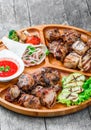 Assorted delicious grilled meat and vegetables with fresh salad and bbq sauce on cutting board on wooden background close up Royalty Free Stock Photo