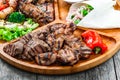 Assorted delicious grilled meat and vegetables with fresh salad and bbq sauce on cutting board on wooden background close up Royalty Free Stock Photo