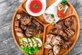 Assorted delicious grilled meat and vegetables with fresh salad and bbq sauce on cutting board on wooden background close up Royalty Free Stock Photo