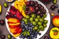 Assorted fresh berries of a cherry, gooseberry, blueberries, slices of ripe peach, plum and apricot, fragrant mint on a plate Royalty Free Stock Photo