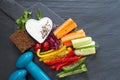 Assorted fresh chopped vegetables with dip and dumbbells on dark background, sport and healthy food concept