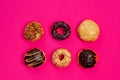 Assorted fresh donuts on a pink background