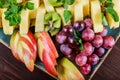 Assorted fresh fruits on plate. Apple, grapes, kiwi, pineapple, grapefruit, orange, banana and mint on wooden table.