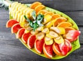 Assorted fresh fruits on plate. Apple, orange, pineapple, grapefruit, banana and mint on dark background.