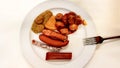 Assorted German sausages on a white plate with a fork in a pub. Traditional German food in a plate. Carrivurst, Bratwurst,