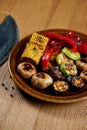 Assorted grilled vegetables - mushrooms, zucchini, peppers, corn in a ceramic plate on a wooden background. Vegetarian warm salad Royalty Free Stock Photo