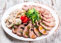 Assorted meat appetizer, cow`s tongue, ham, stuffed chicken roll, meat roll with pepper, greens on plate over rustic background Royalty Free Stock Photo