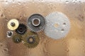 Assorted metal gears on glass, with water drops or condensation, wood background