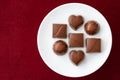 Assorted milk chocolate candy on a white plate on a red background