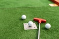 Assorted miniature golf putters and balls askew on synthetic grass.