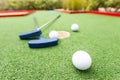 Assorted miniature golf putters and balls askew on synthetic grass.