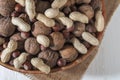 Assorted groundnuts, walnuts and hazelnuts. Nuts in a bowl on burlap. White wooden background. Close-up