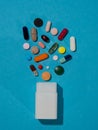 Assorted pharmaceutical medicine pills, tablets and capsules and white bottle on blue background. Royalty Free Stock Photo