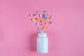 Colored pills, tablets and white bottle on pink background