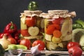 Assorted pickled cucumbers, patissons, peppers, zucchini and tomatoes in jars on a dark background, horizontal format