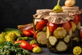 Assorted pickled cucumbers, patissons and tomatoes in jars on a dark background, horizontal orientation, copy space Royalty Free Stock Photo