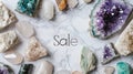 Assorted precious gemstones and crystals, including amethyst and quartz, form a luxurious frame around a Sale sign on a