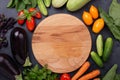 Assorted raw organic vegetables and cutting board on dark stone background Royalty Free Stock Photo