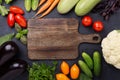 Assorted raw organic vegetables and cutting board on dark stone background Royalty Free Stock Photo