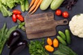 Assorted raw organic vegetables and cutting board on dark stone background Royalty Free Stock Photo