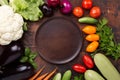 Assorted raw organic vegetables and empty plate on dark stone background Royalty Free Stock Photo