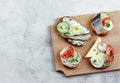 Assorted sandwiches with vegetables and fish on the wooden cutting board on a light gray background