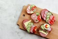 Assorted sandwiches with vegetables and sausages on the wooden cutting board on a light gray background