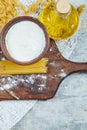 Assorted scattered uncooked pasta, a bottle of oil and a bowl of flour