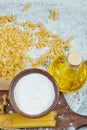 Assorted scattered uncooked pasta, a bottle of oil and a bowl of flour