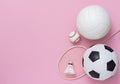 Assorted sports equipment including a basketball, soccer ball, volleyball, baseball, badminton racket on a pink background