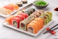 Assorted sushi rolls on a white square dish, seaweed salad and chopsticks on a white stone