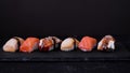 Assorted sushi with salmon, eel and escolar move on a black plate on dark background. Minimal concept