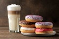 Assorted sweet donuts with icing and toppings, and coffee latte on a brown wooden table Royalty Free Stock Photo