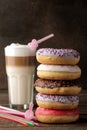 Assorted sweet donuts with icing and toppings, and coffee latte on a brown wooden table Royalty Free Stock Photo