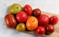 Assorted tomatoes on a rectangular cutting wooden board on a light gray background