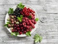 Assortment of berries - raspberries, gooseberries, red currants, cherries, black currants on a white plate on a wooden background. Royalty Free Stock Photo