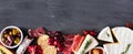 Assortment of cheese and meat appetizers, bottom border on a slate stone banner background