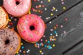 Assortment of colorful donuts decorated with colorful confetti sprinkles on dark wooden background Royalty Free Stock Photo