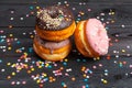 Assortment of colorful donuts decorated with colorful confetti sprinkles on dark wooden background Royalty Free Stock Photo