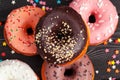 Assortment of colorful donuts decorated with colorful confetti sprinkles on dark wooden background Royalty Free Stock Photo