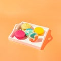 Assortment of colorful macaroons on wooden tray on orange background with sunlit. Dessert concept