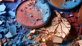 Assortment of cracked eyeshadow powders in blue, brown, and red hues, artistically scattered and creating a vibrant, textured