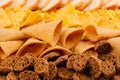 Assortment crunchy snacks - popcorn, nachos, croutons, corn sticks, potato chips as decorative stripes background, closeup