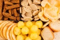 Assortment crunchy snacks - popcorn, nachos, croutons, corn sticks, potato chips in cells as decorative background, top view.