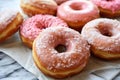 An assortment of donuts with pink and white icing, some decorated with colorful sprinkles and others with a dusting of