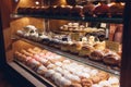 Assortment of doughnuts on cafe showcase. Variety of desserts with different flavours on shelves in store.