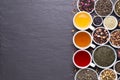 Assortment of dried tea leaves, fruit and herbs in bowls on dark, stone background