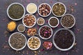 Assortment of dried tea leaves, fruit and herbs in bowls on dark, stone background