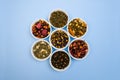 Assortment of dry tea in bowls on blue background. Flat lay style. Healthy, organic drink
