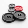 Assortment of Four Sewing Buttons Including Two Large Black, One Medium Black, and One Red Button on a White Surface Royalty Free Stock Photo